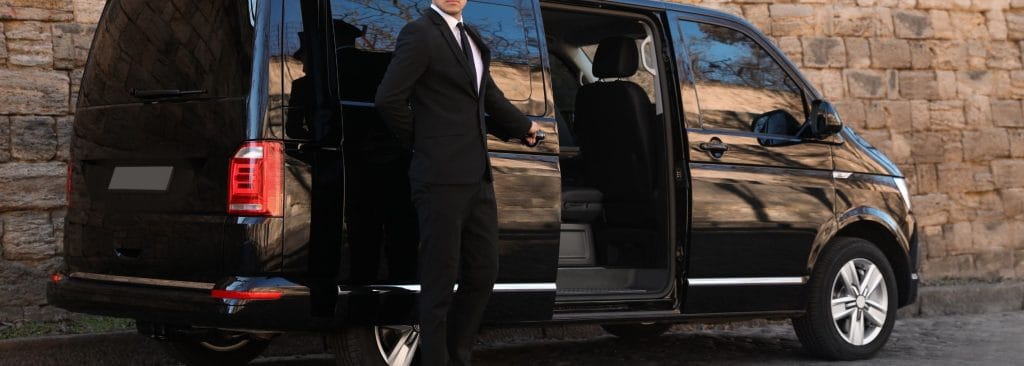 Professional event chauffeur standing beside a luxury vehicle, waiting for a client to exit the function venue.