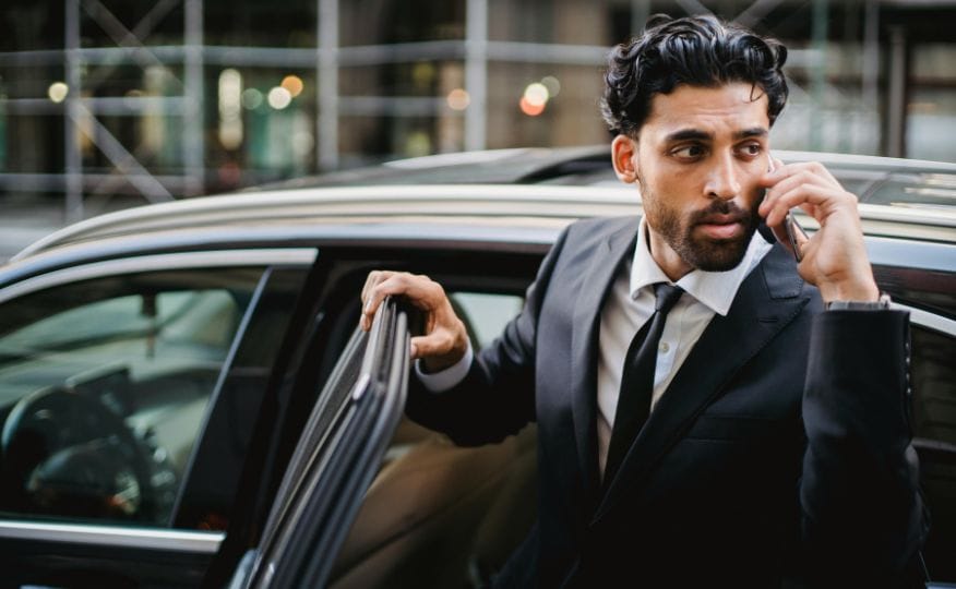 A client stepping out of a chauffeur vehicle while on the phone